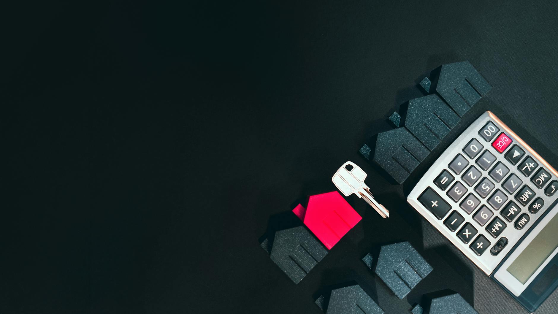 Kalkulator, miniaturowe domy i klucz na ciemnym tle